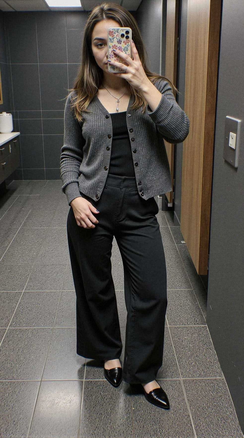 A woman posing in a grey ribbed knit cardigan, black top, and black wide-leg trousers.