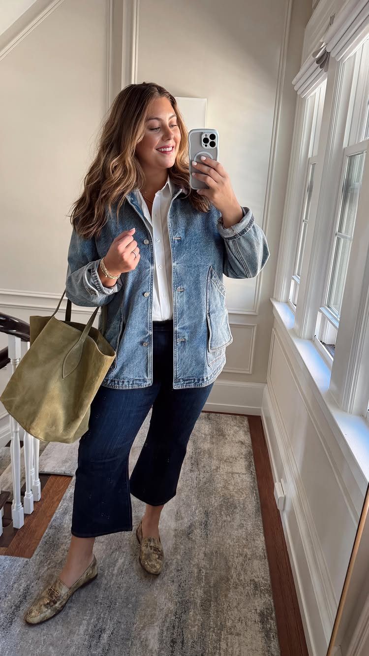 A woman posing in a mirror wearing a denim jacket, white shirt, and dark wide-leg jeans.