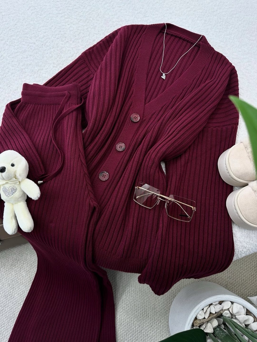 Burgundy ribbed knit cardigan and matching pants laid out with accessories on a white surface.