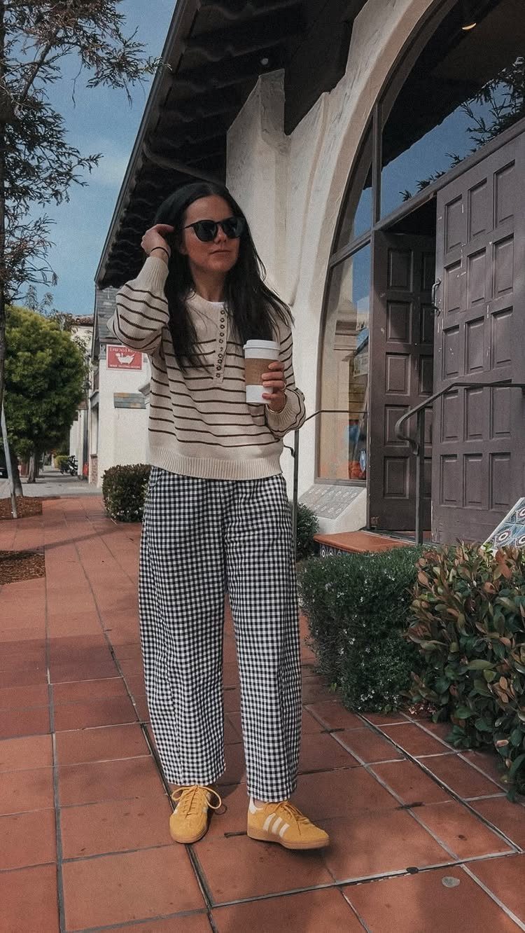 Woman wearing a striped sweater and checkered wide-leg pants standing outdoors with a coffee cup.