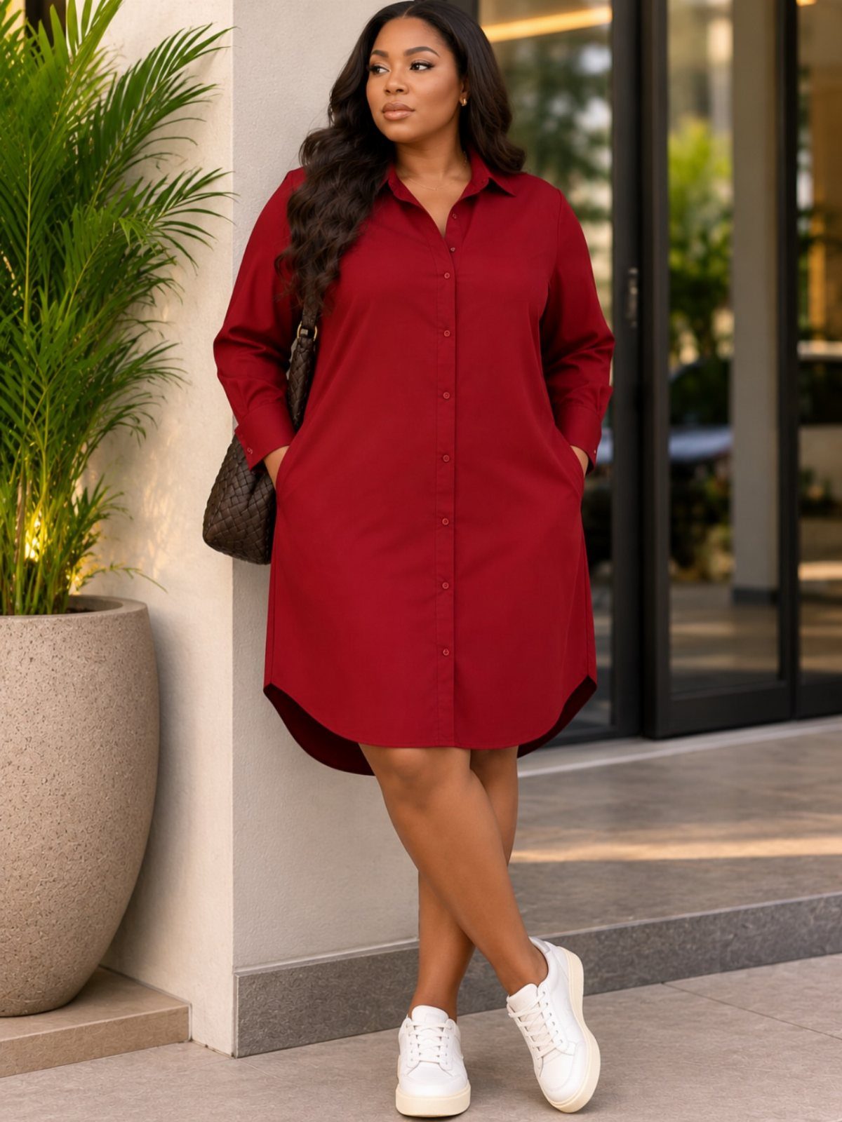 A woman wearing a long-sleeved red cotton shirtdress and white sneakers standing outdoors.