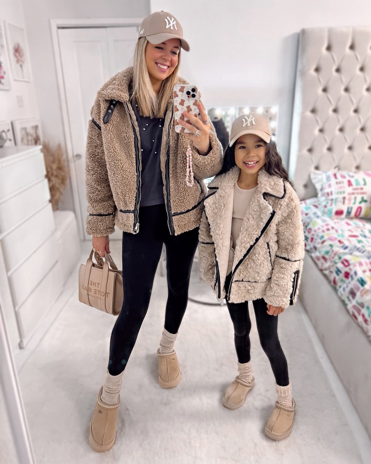 A woman and a young girl wearing tan sherpa jackets, black leggings, and tan baseball caps.