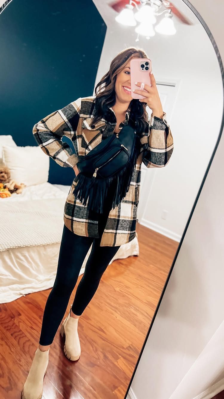 Woman posing in a mirror wearing a plaid shacket, black leggings, and tan ankle boots.