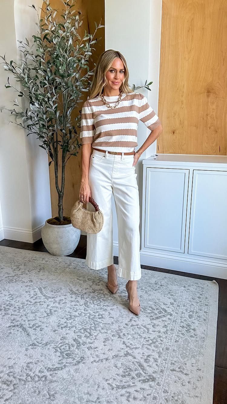 A woman in a striped top and white wide-leg pants posing indoors.