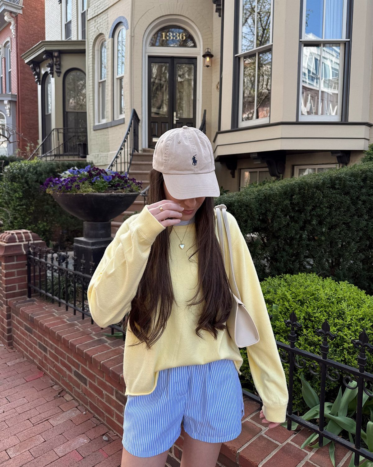 A person wearing a yellow sweatshirt and blue striped shorts standing by a brick wall.