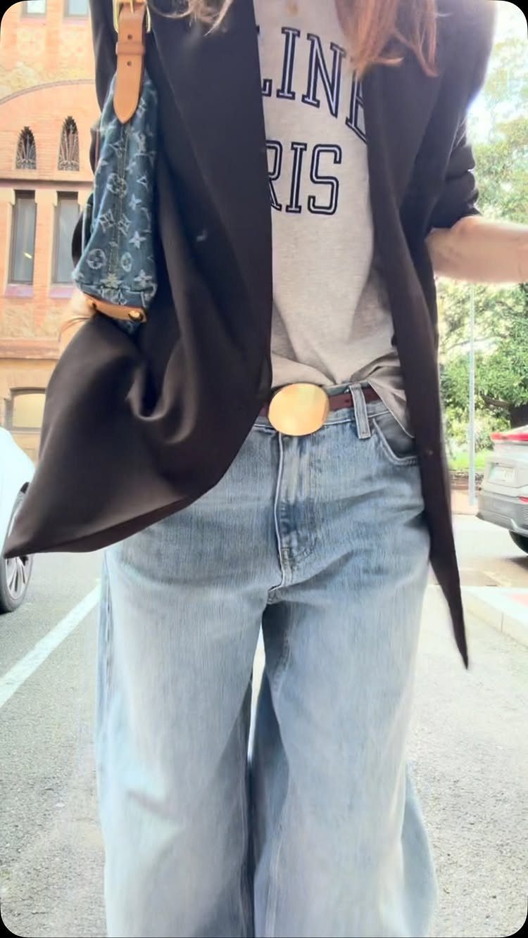 Woman wearing a graphic t-shirt, wide-leg denim jeans, and a dark blazer outdoors.