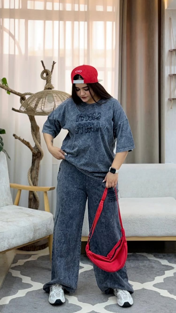 Woman wearing a dark grey oversized t-shirt and matching wide-leg trousers with a red cap.