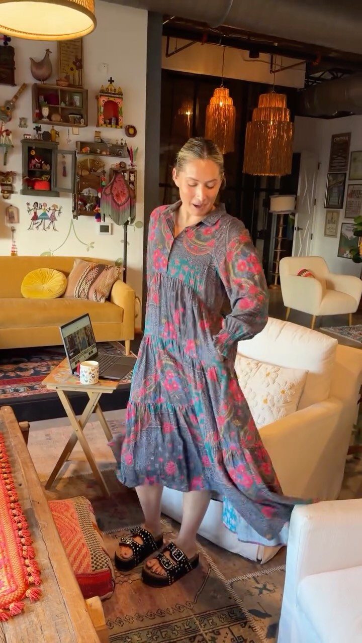A woman wearing a long, patterned grey floral midi dress standing in a living room.