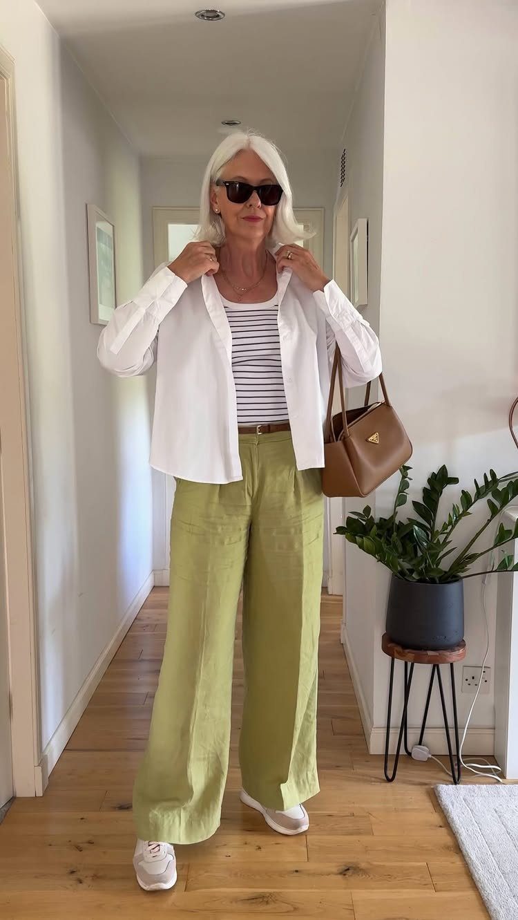 Woman with white hair wearing a white shirt, striped top, and green wide-leg trousers.