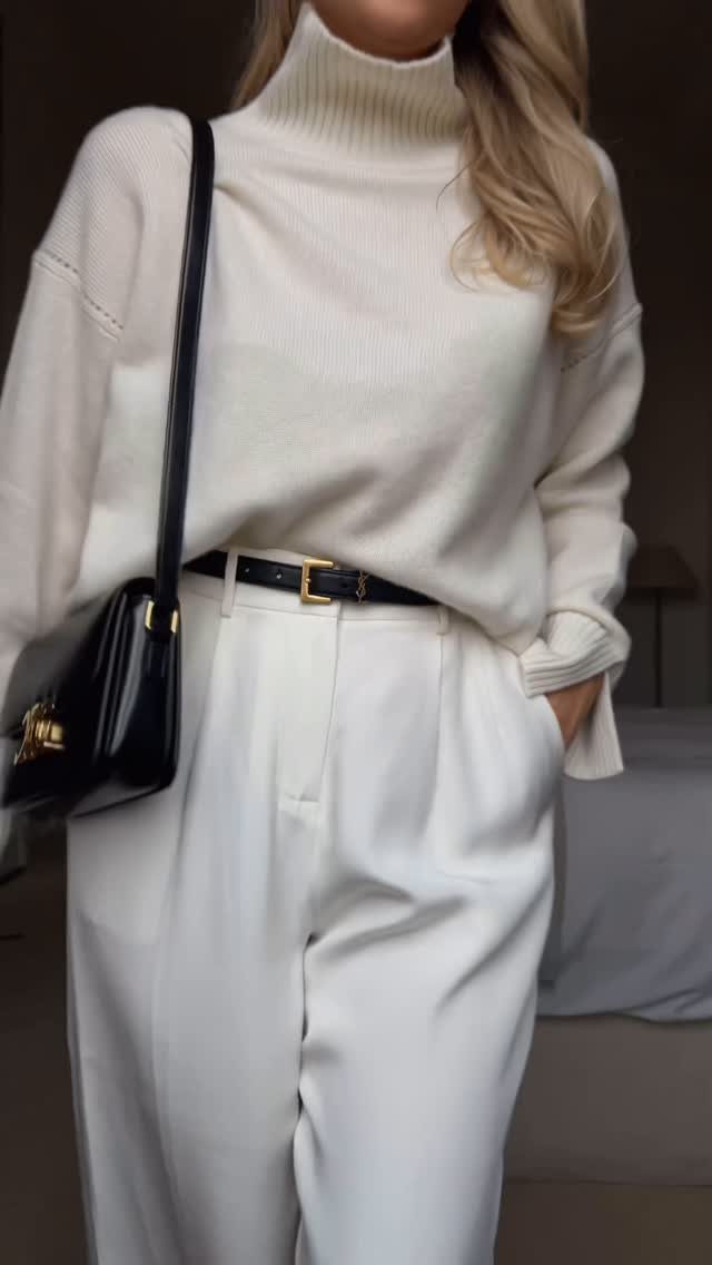 Woman wearing a cream turtleneck sweater and matching high-waisted trousers with a black belt.