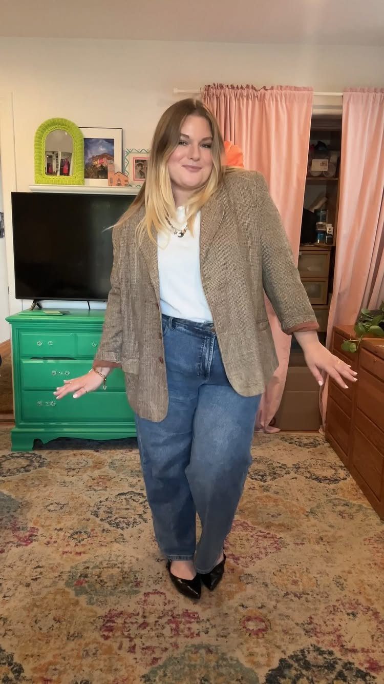 A woman posing in a brown blazer, white t-shirt, and blue straight-leg jeans.