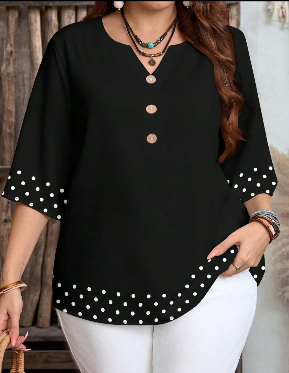 Woman wearing a black polka dot blouse with wooden buttons and white trousers.