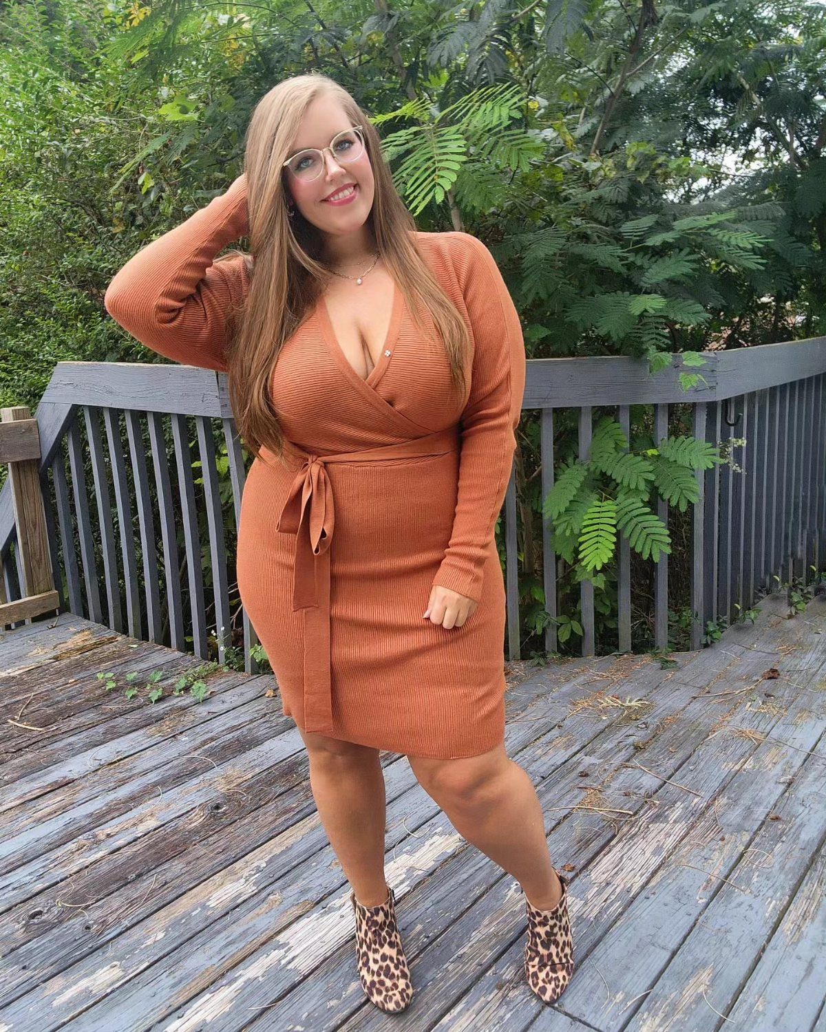 A woman in a burnt orange ribbed wrap dress and leopard print boots standing on a wooden deck.