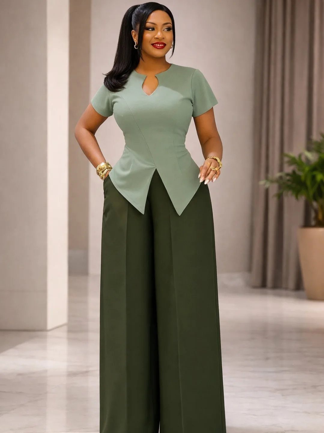 A woman posing in a sage green blouse and dark olive wide-leg trousers.