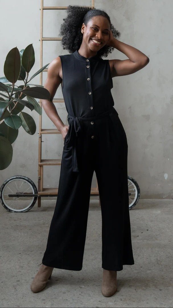 A smiling woman posing in a black sleeveless wide-leg jumpsuit against a neutral background.