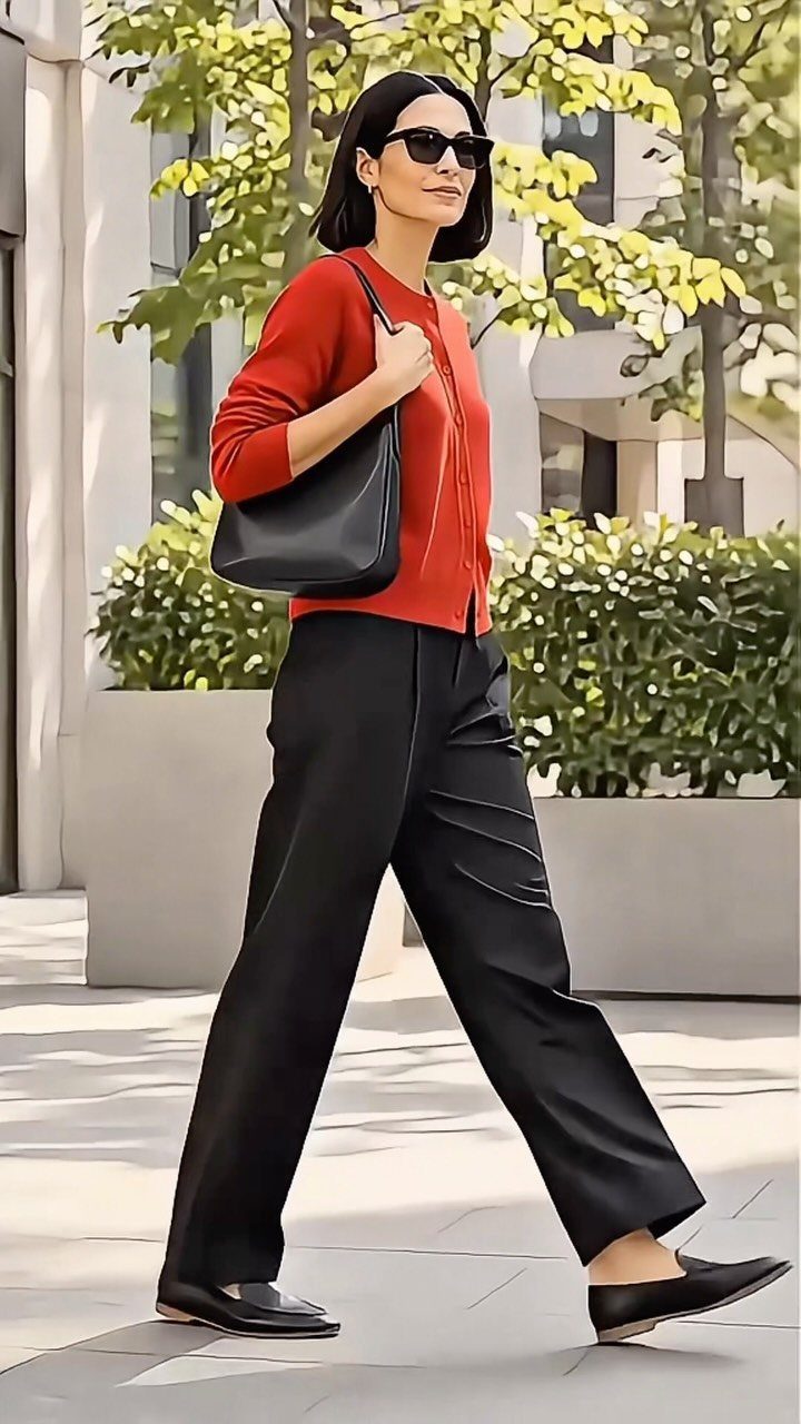 Woman walking in a red top, black wide-leg trousers, and black loafers.