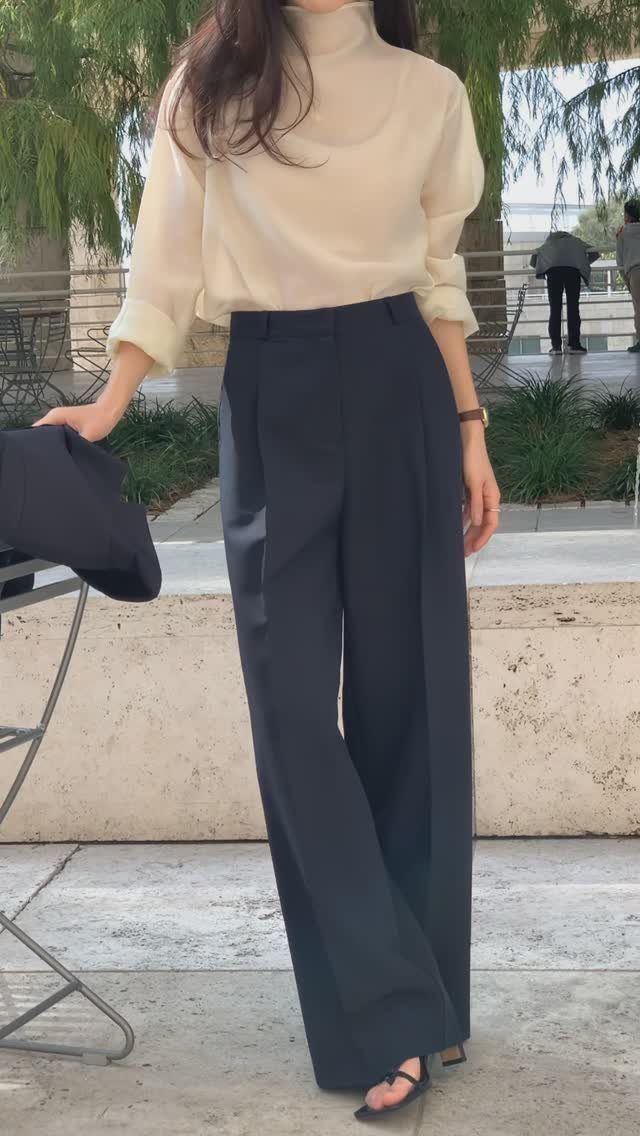 Person wearing a cream turtleneck blouse and navy wide-leg trousers standing outdoors.