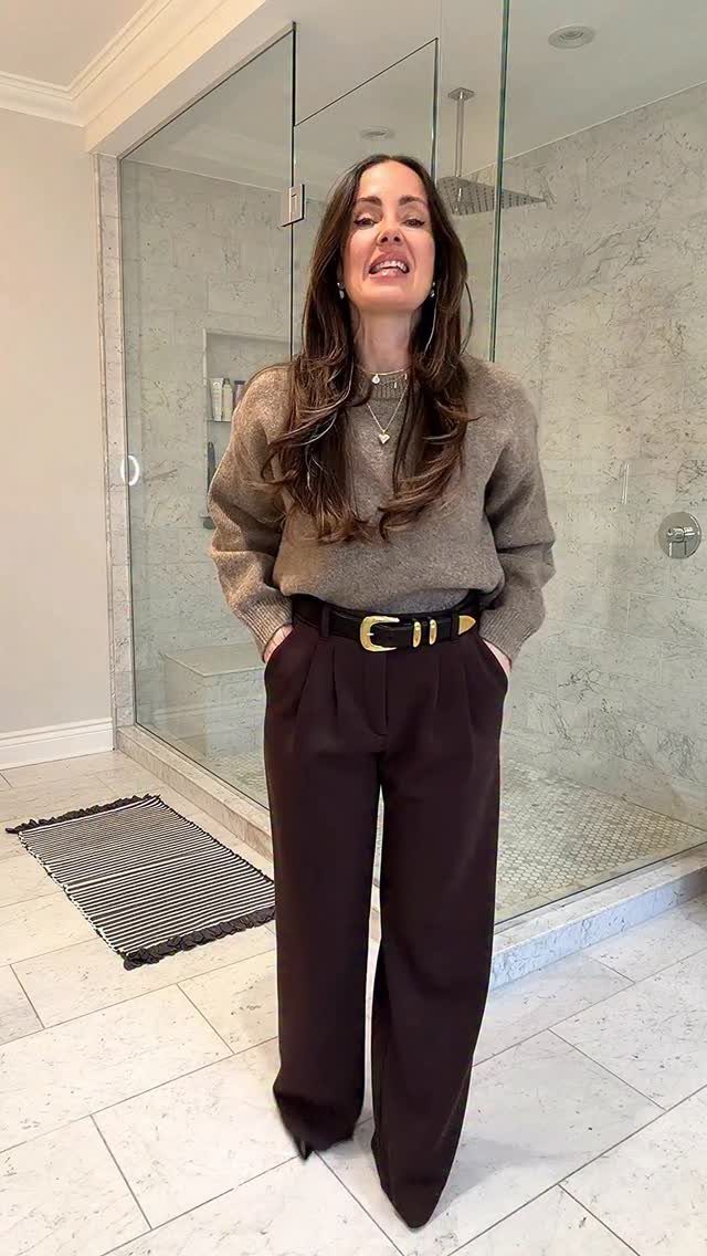 A woman posing in a brown sweater and dark brown high-waisted wide-leg trousers.
