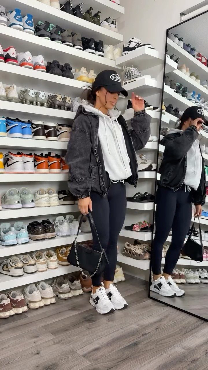 Woman in a sporty outfit posing in a room filled with many rows of sneakers.