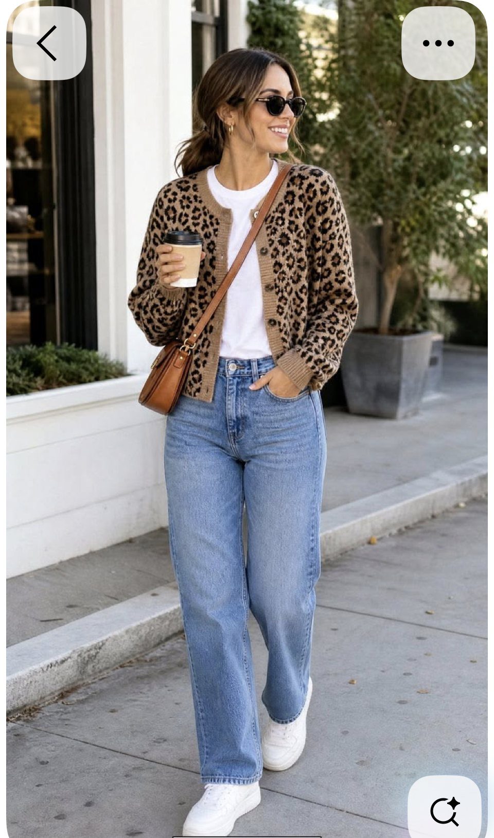 A woman in a leopard print cardigan and blue jeans walking outdoors while carrying a brown leather bag.