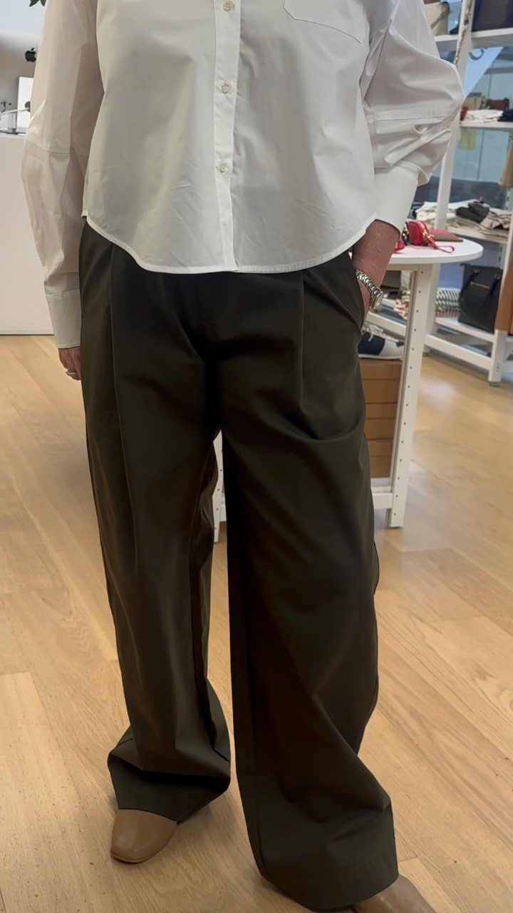 Person wearing a white button-up shirt and wide-leg dark olive green tailored trousers.