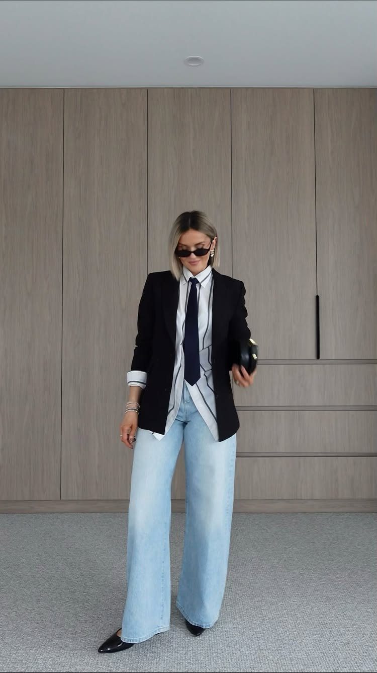 Woman posing in a black blazer, striped shirt, and light blue wide-leg denim jeans.