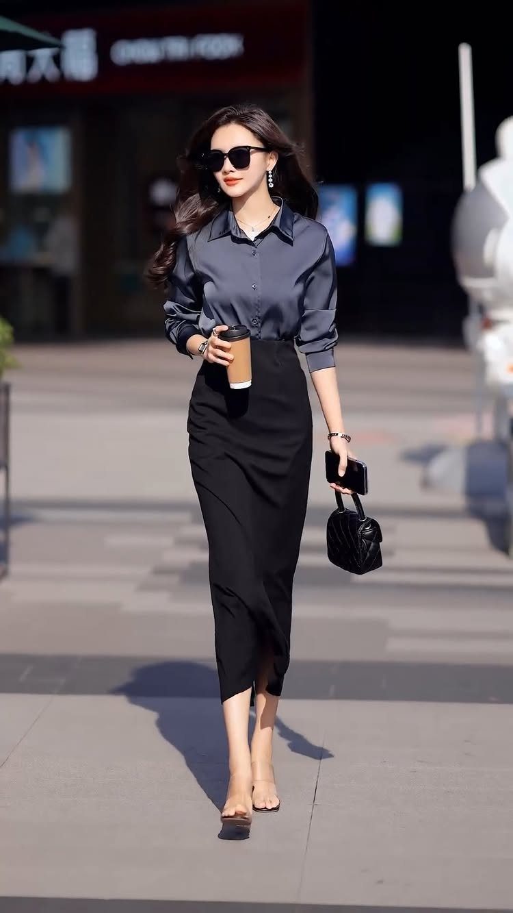 Woman walking in a dark grey button-down shirt and a black midi skirt.