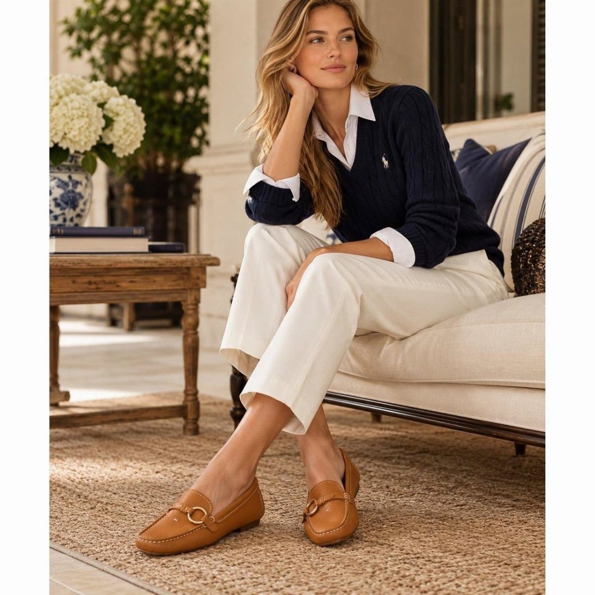 Woman sitting on a sofa wearing white trousers and tan leather loafers.