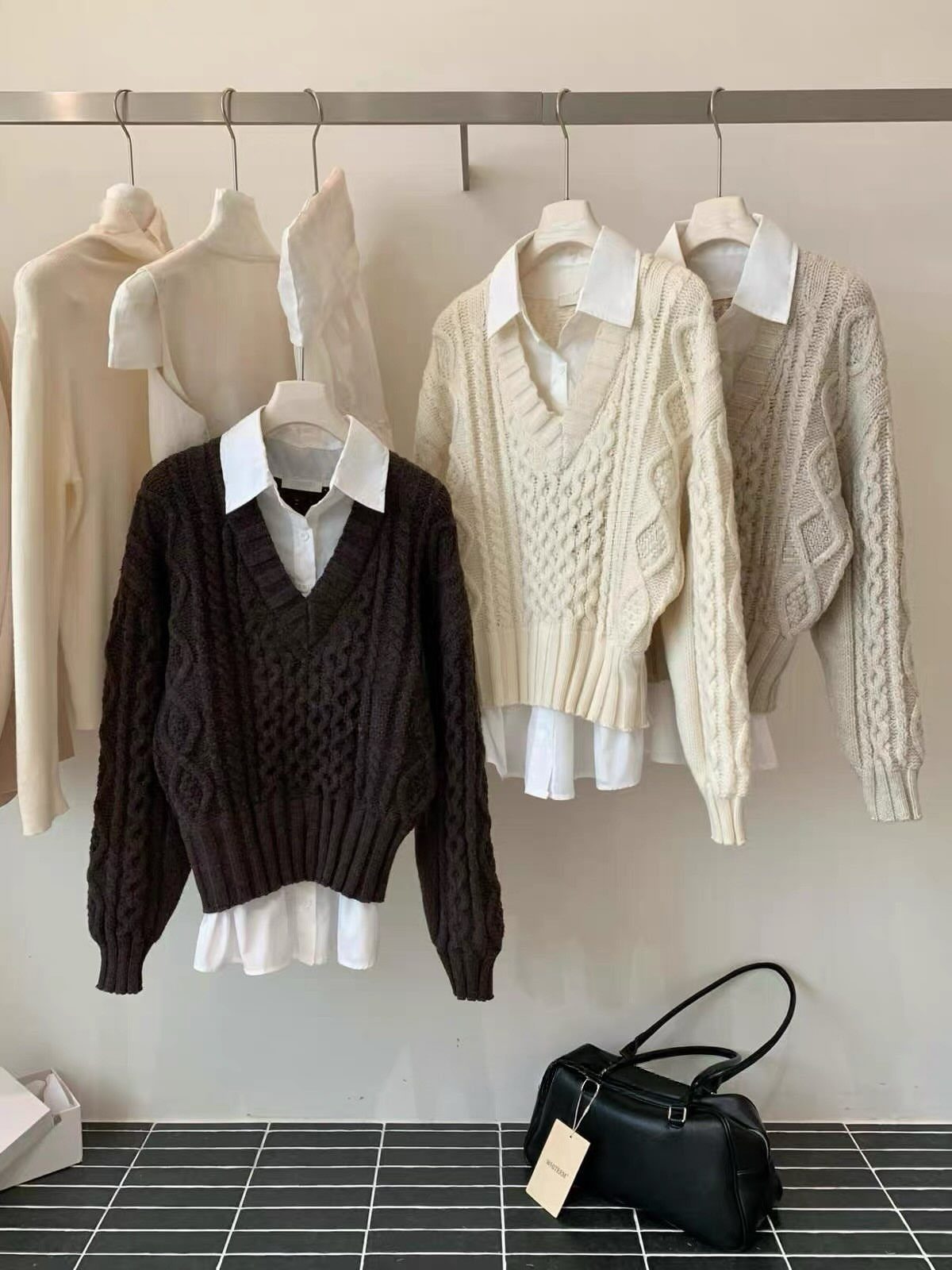 Knitted sweaters layered over white collared shirts hanging on a metal clothing rack.