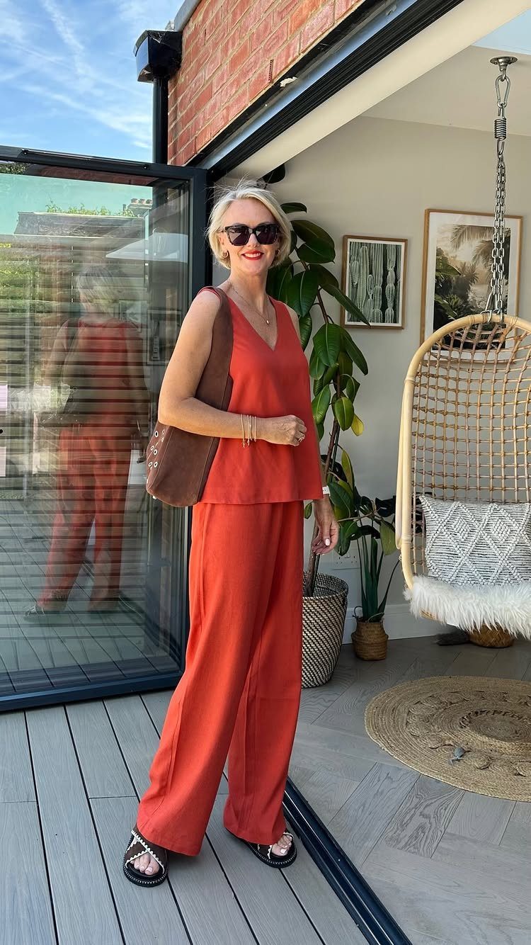 Woman in a burnt orange linen sleeveless top and wide-leg trousers standing on a patio.