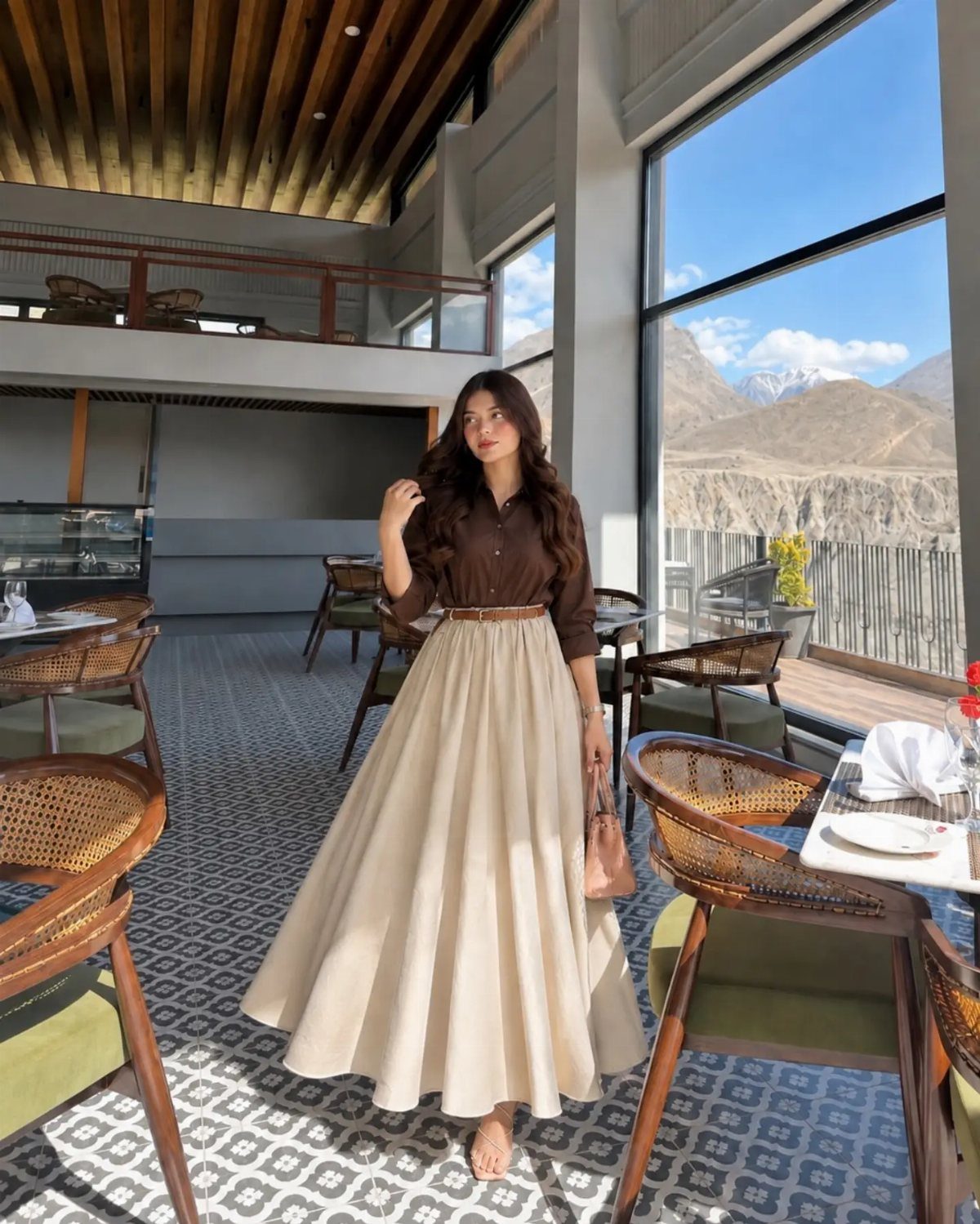 A woman wearing a long cream maxi skirt and brown shirt standing in a restaurant.
