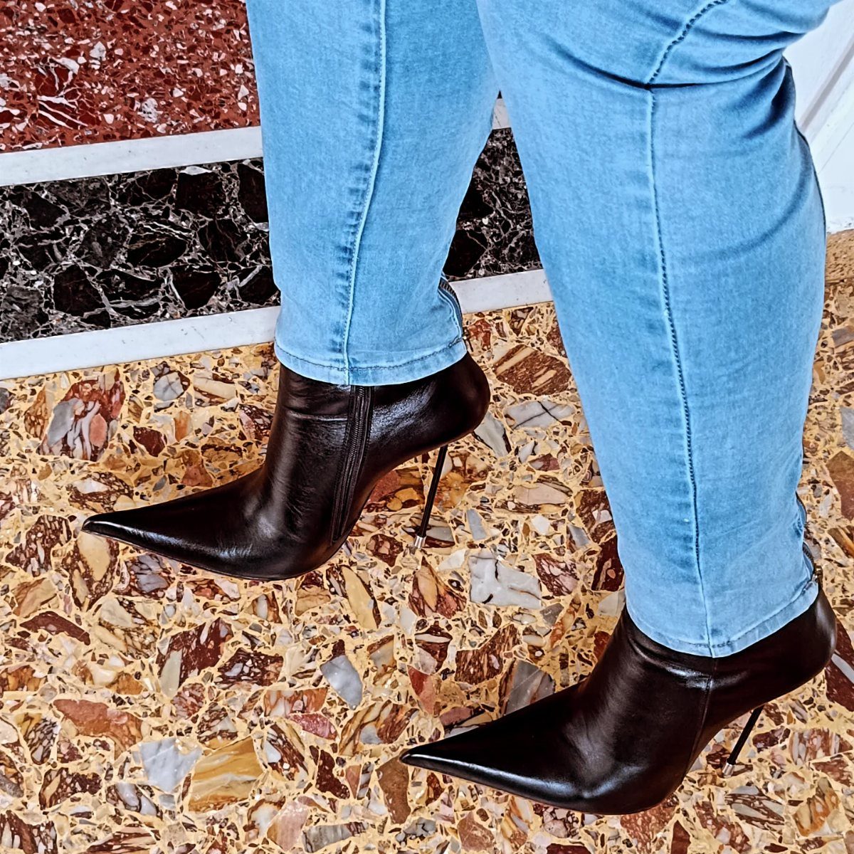 Black leather stiletto ankle boots with pointed toes worn with light blue denim jeans.