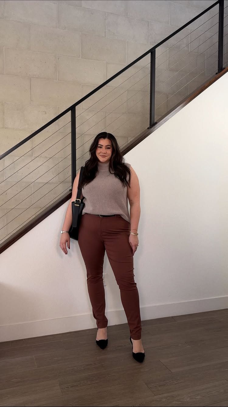 A woman posing in a sleeveless knit top, reddish-brown trousers, and black heels.