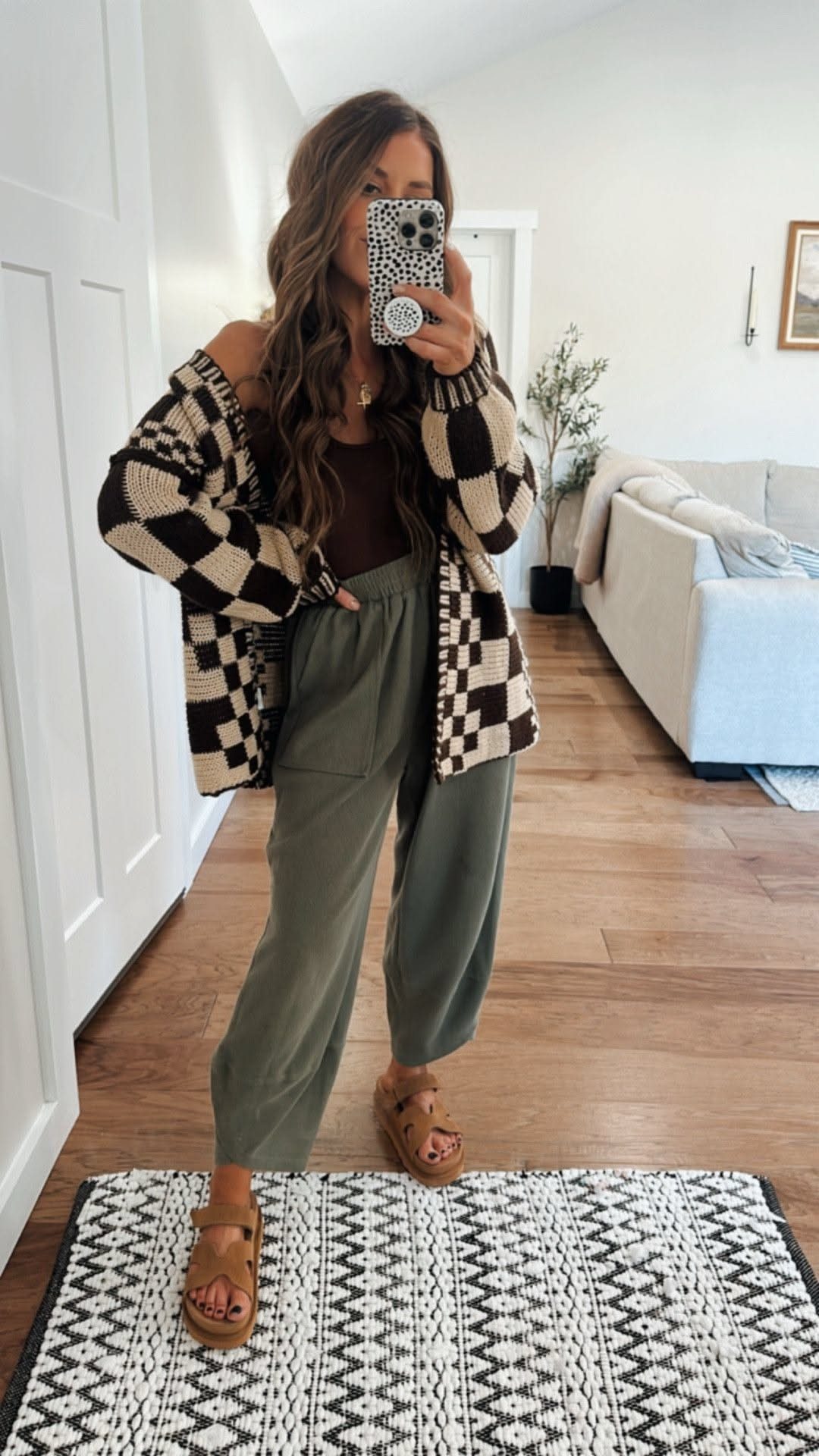 Woman in a checkered cardigan and olive green wide-leg pants posing for a mirror selfie.
