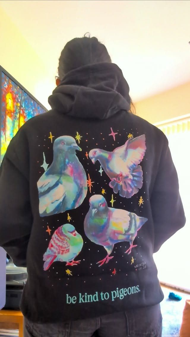 A person wearing a black hoodie with colorful pigeon graphics and text on the back.