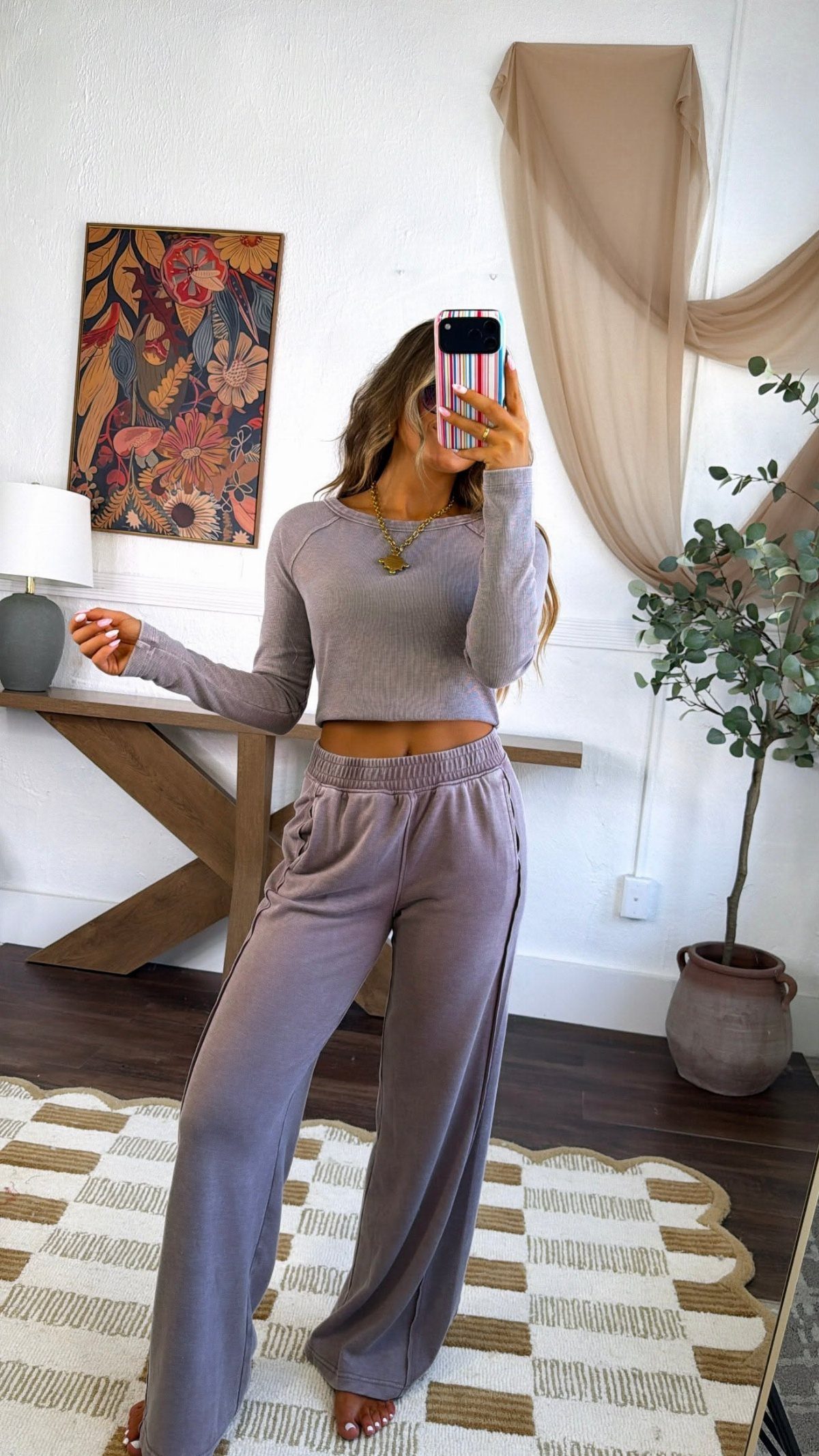 Woman in a mauve matching lounge set posing for a mirror selfie in a living room.