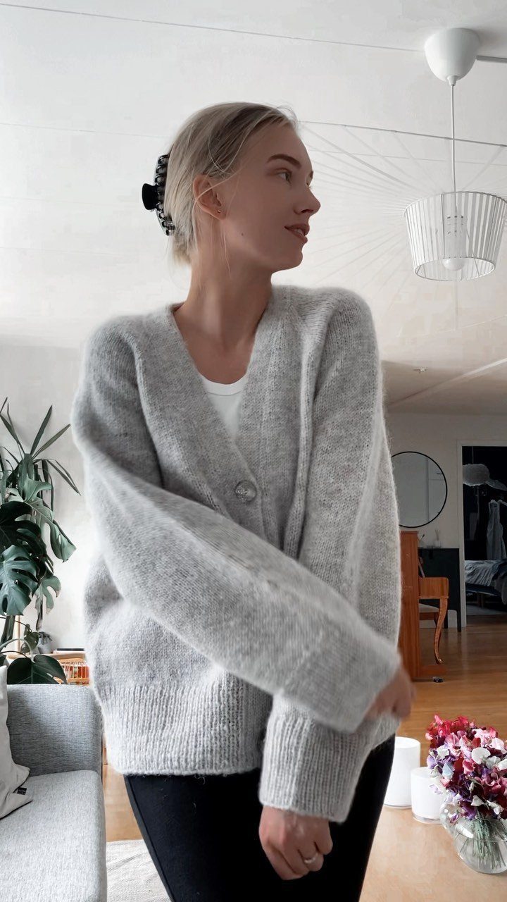 A blonde woman wearing a grey oversized fuzzy knit cardigan in a bright room.