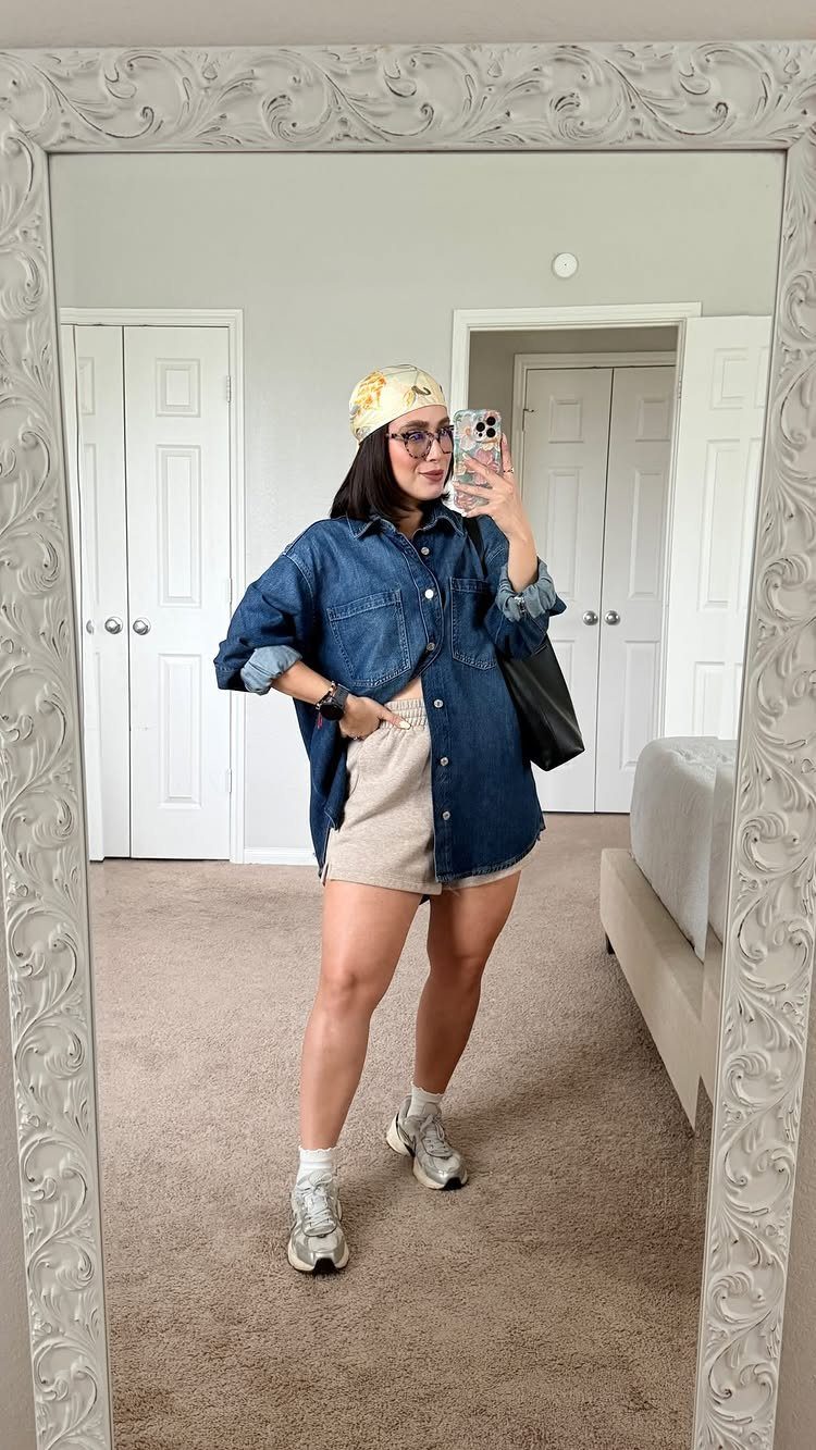 Woman in denim shirt and tan shorts posing for a mirror selfie with accessories.