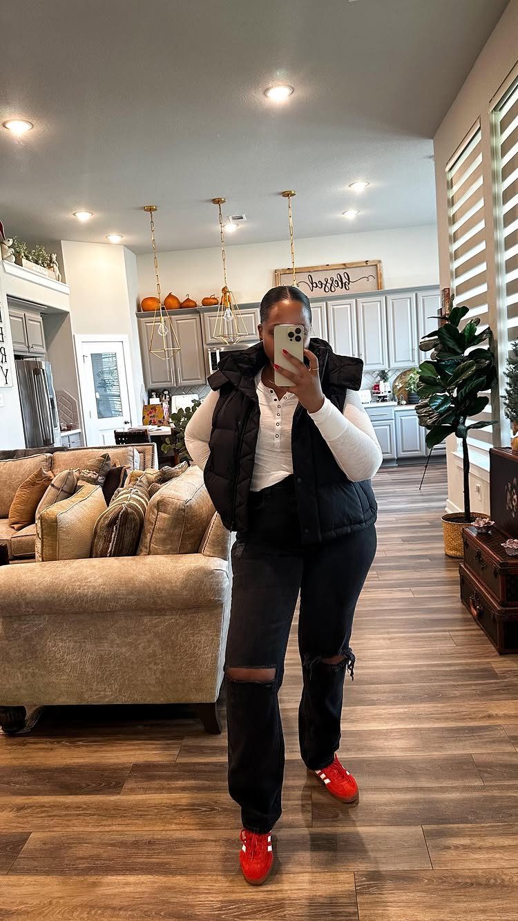 Woman in black puffer vest and ripped jeans wearing bright red casual sneakers.
