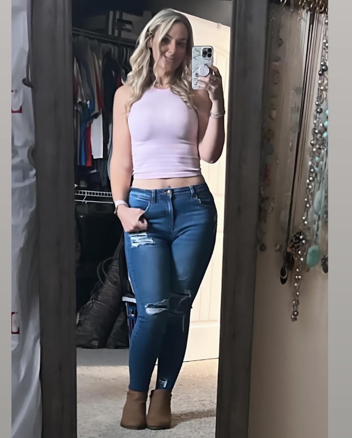 A blonde woman posing in a pink cropped top and blue distressed jeans.