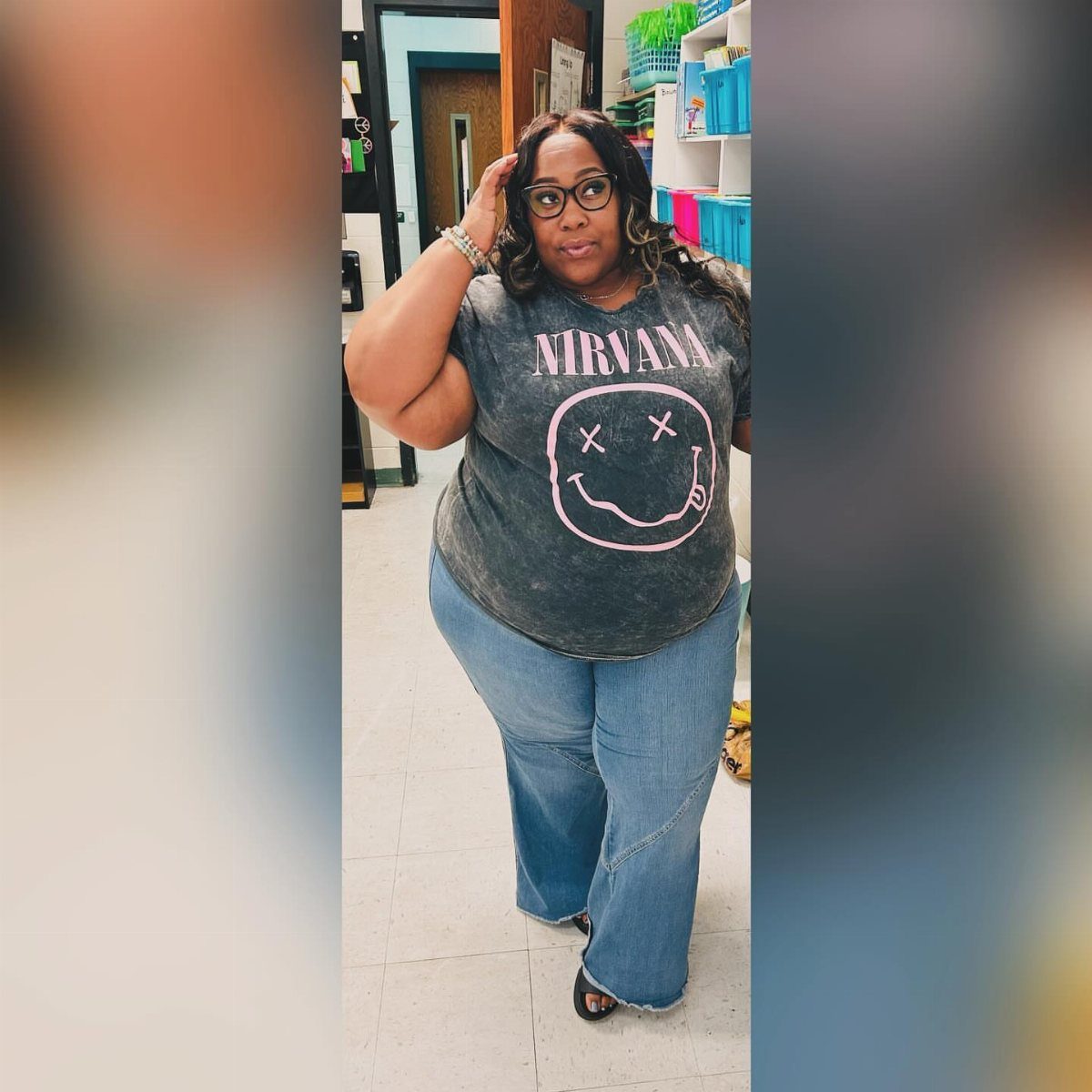 A woman wearing a Nirvana graphic t-shirt and wide-leg blue jeans standing indoors.