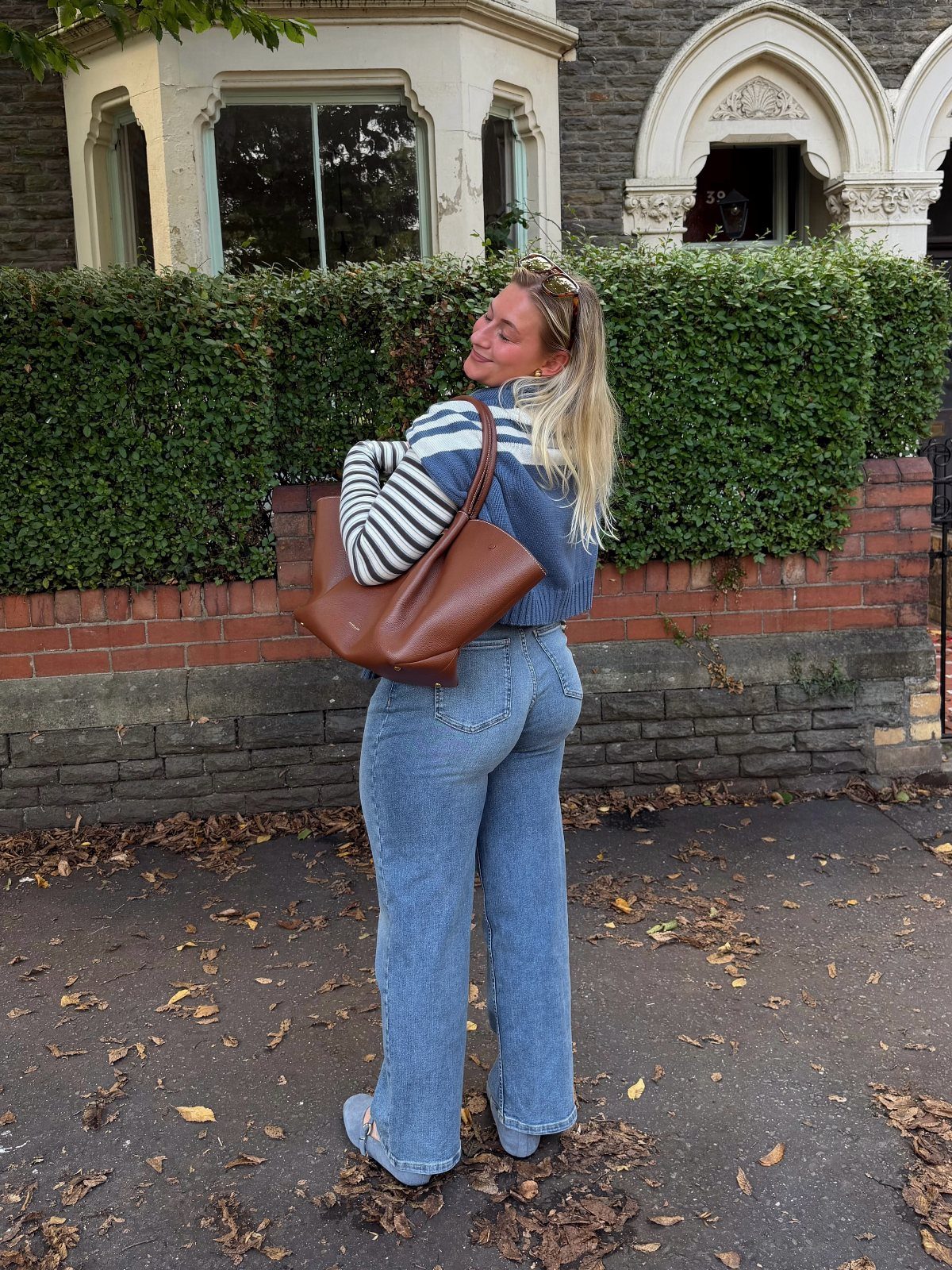 A woman wearing blue striped sweater and high-waisted wide-leg denim jeans standing outdoors.