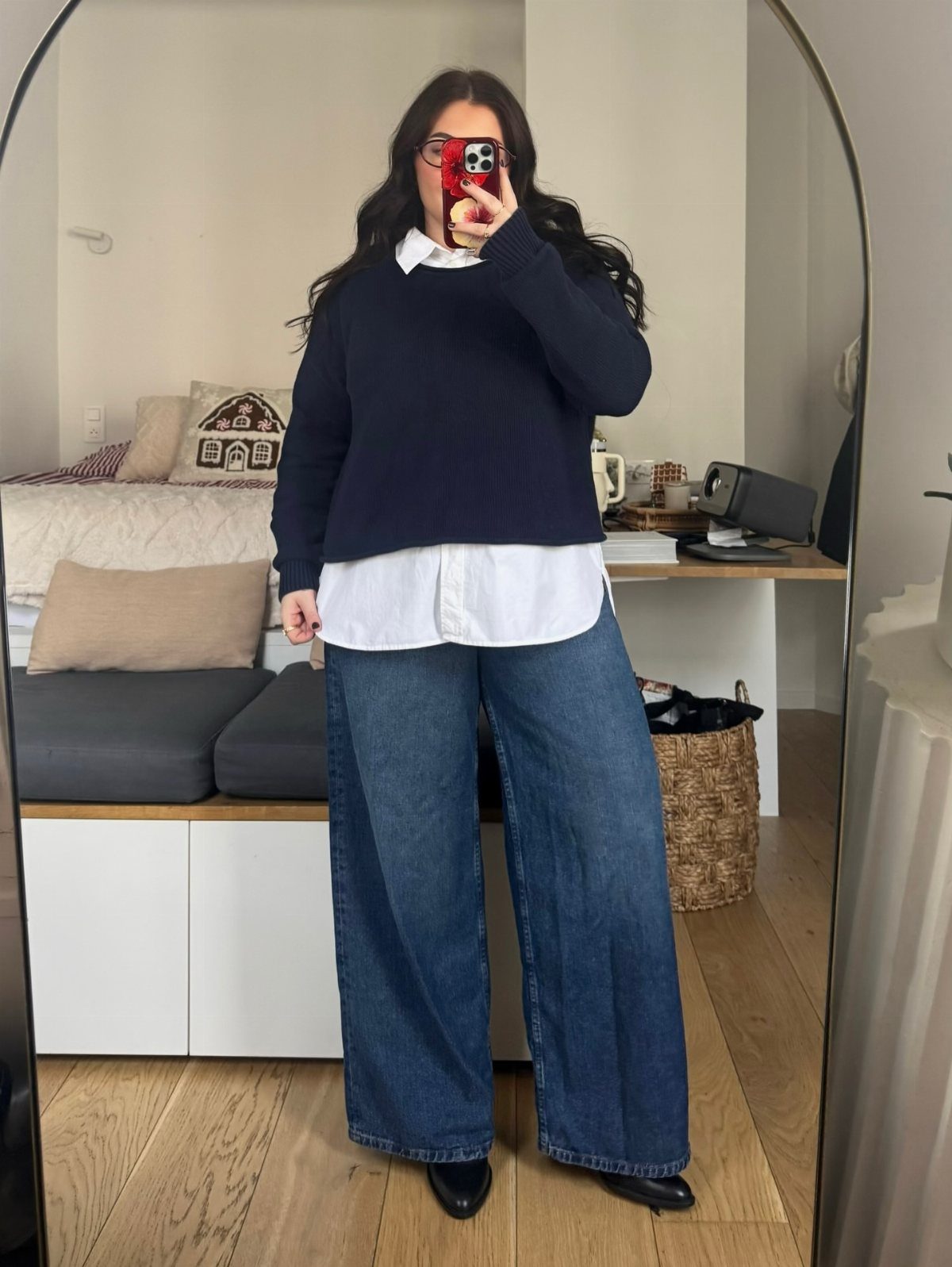 Woman in a navy sweater layered over a white shirt and wide-leg denim jeans.