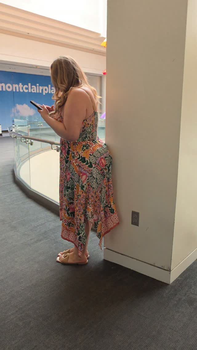 A woman in a floral maxi dress stands in a hallway looking at her phone.