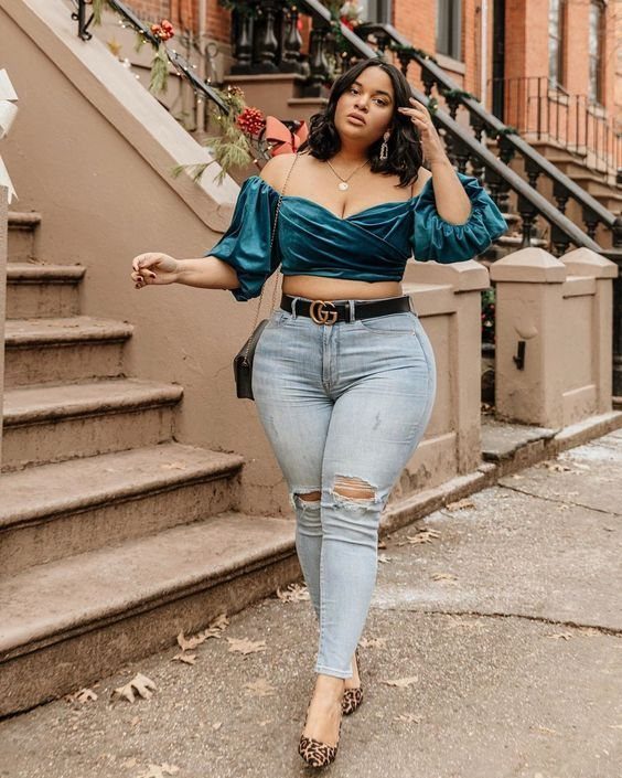 Woman in a teal puff sleeve crop top and ripped light blue jeans posing outdoors.