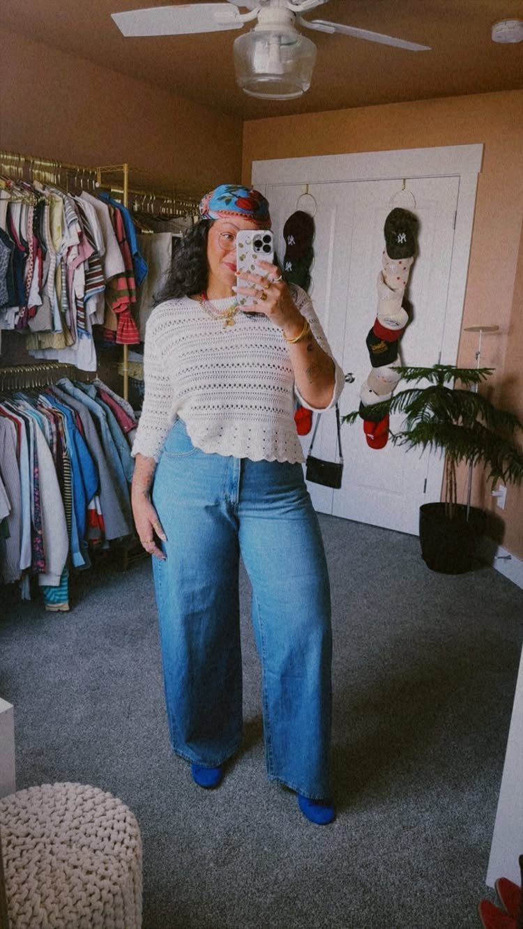 Woman in a white crochet top and wide-leg blue denim jeans posing for a selfie.