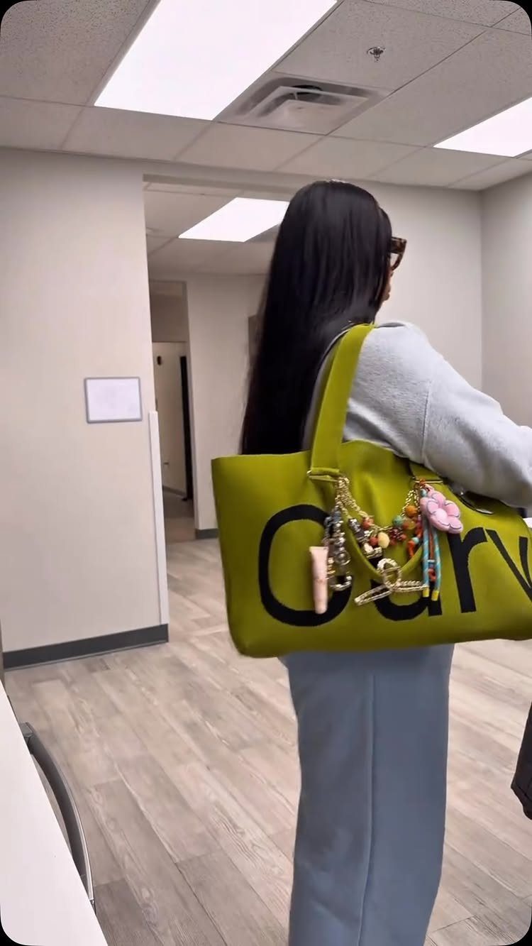 A person carrying a large lime green tote bag decorated with colorful charms and keychains.