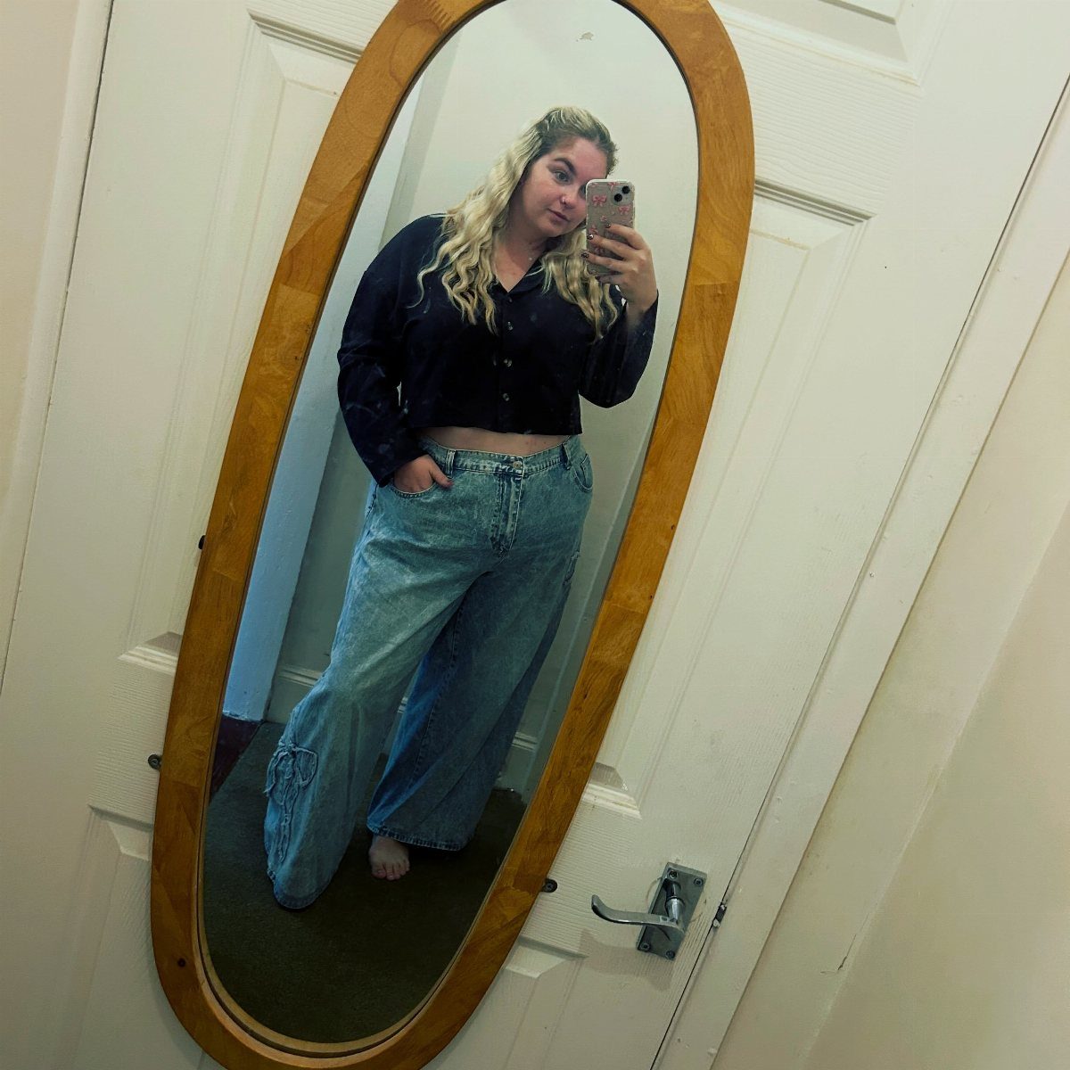 A woman in a black shirt and wide-leg jeans posing for a mirror selfie.