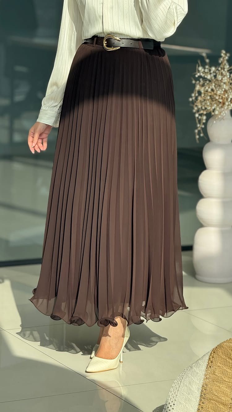 A person wearing a long dark brown pleated skirt, a cream blouse, and cream heels.