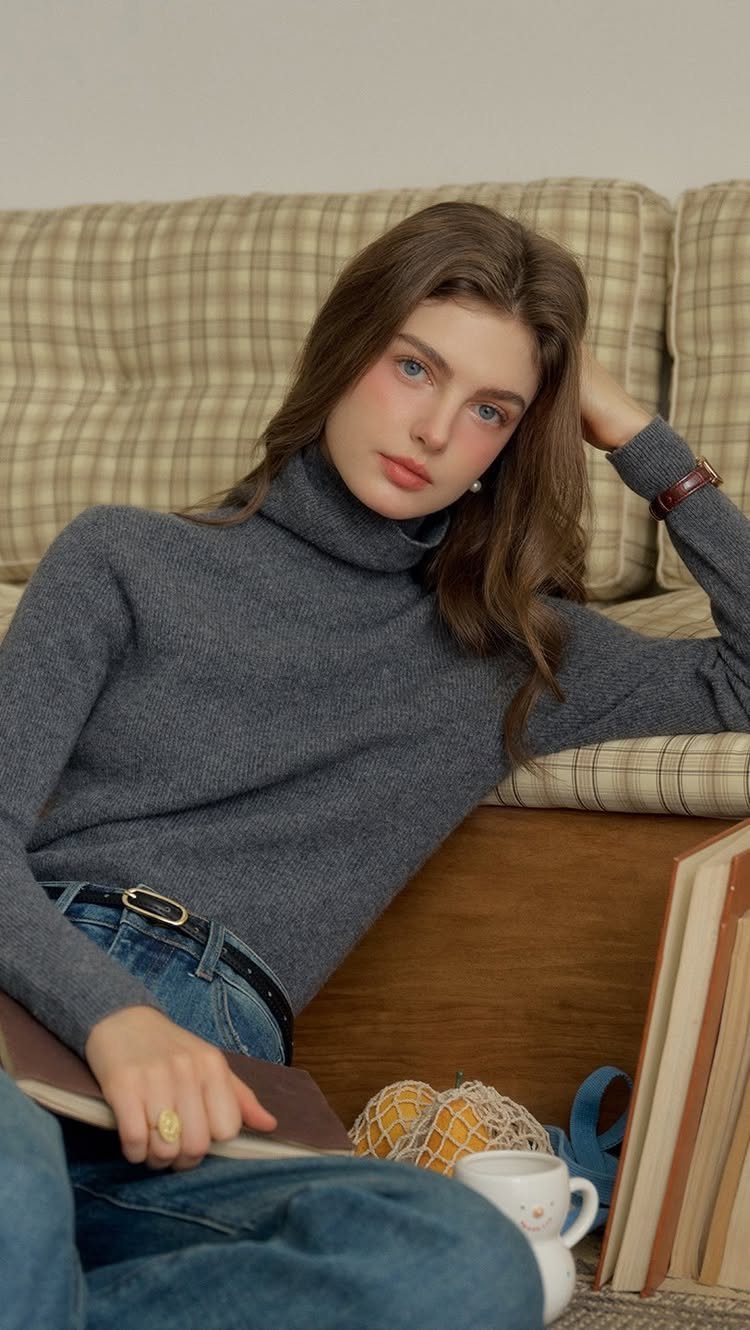 A woman wearing a grey cashmere turtleneck sweater sitting on a plaid sofa.